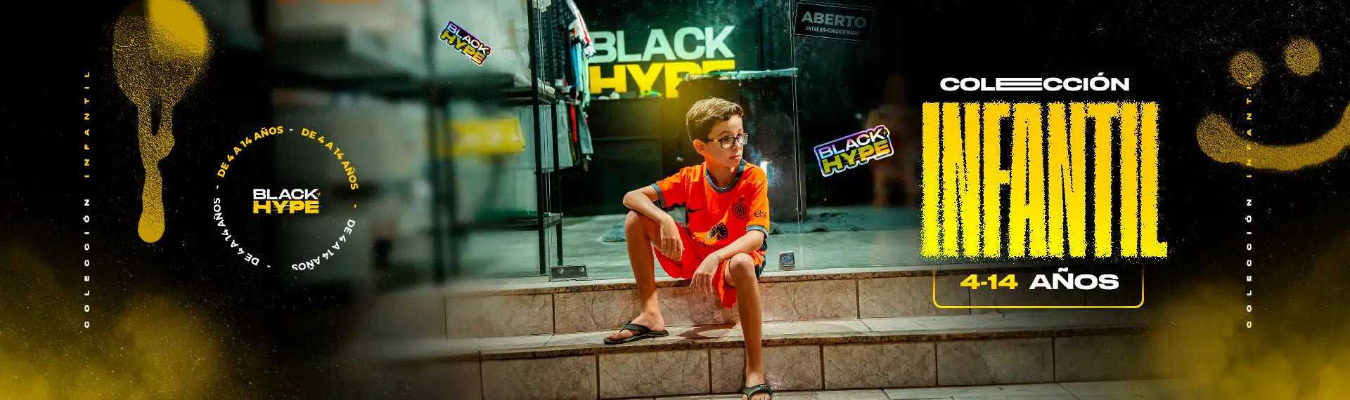Un niño pequeño con una camisa naranja y shorts se sienta en unos escalones, usando gafas.